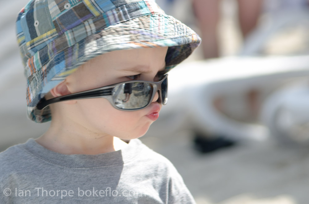 An image of a 3 year old wearing sunglasses in a unique way