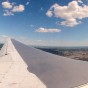 GoPro photograph from inside a flying airplane looking out over the wing to the horizon with the clouds above and the land below