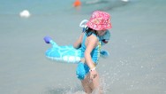 A medium shot of a 5 year old beach girl with bucket hat, and a floating toy, wading into the waves at the beach with the waves and water background at the Iberostar Laguna Azul Beach Resort in Varadero Cuba