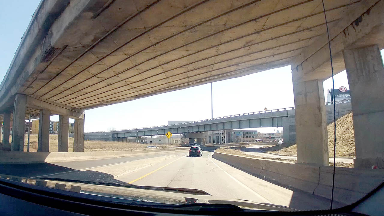 The photograph is a view through the windsheild the GoPro Hero 4 Black camera is mounts to with the GoPro suction cup, outward of the highway with another car and going under an over pass in Montreal.