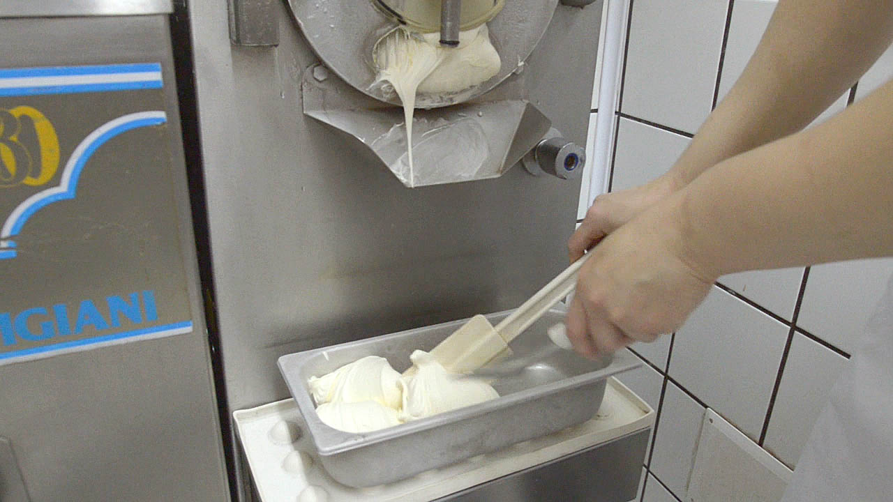 Gelato from a gelato machine starts to fill up a gelato tub a scoop at a time Sorrento Italy