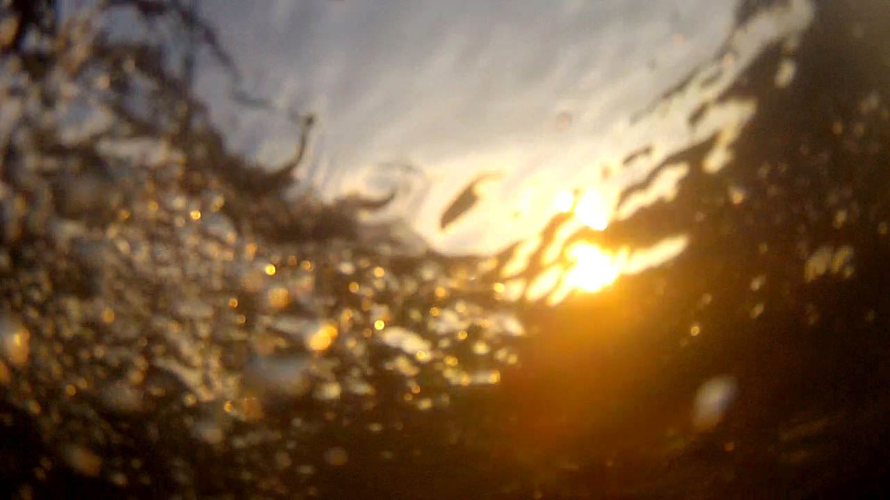 The photograph shows the sun and the sky from a GoPro camera slightly below the surface of the water with the bubble from the wake wave off to one side.
