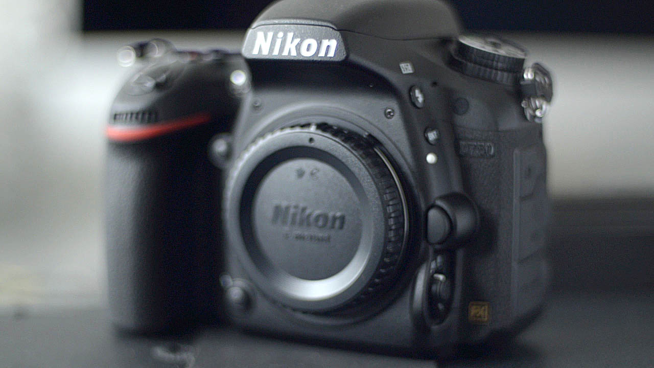 The photograph is a close up of the Nikon D750 camera body on a slight angle. The D750 word mark on the Nikon D750 camera body is dark and obscured but Nikon word mark on the camera is plainly visable.