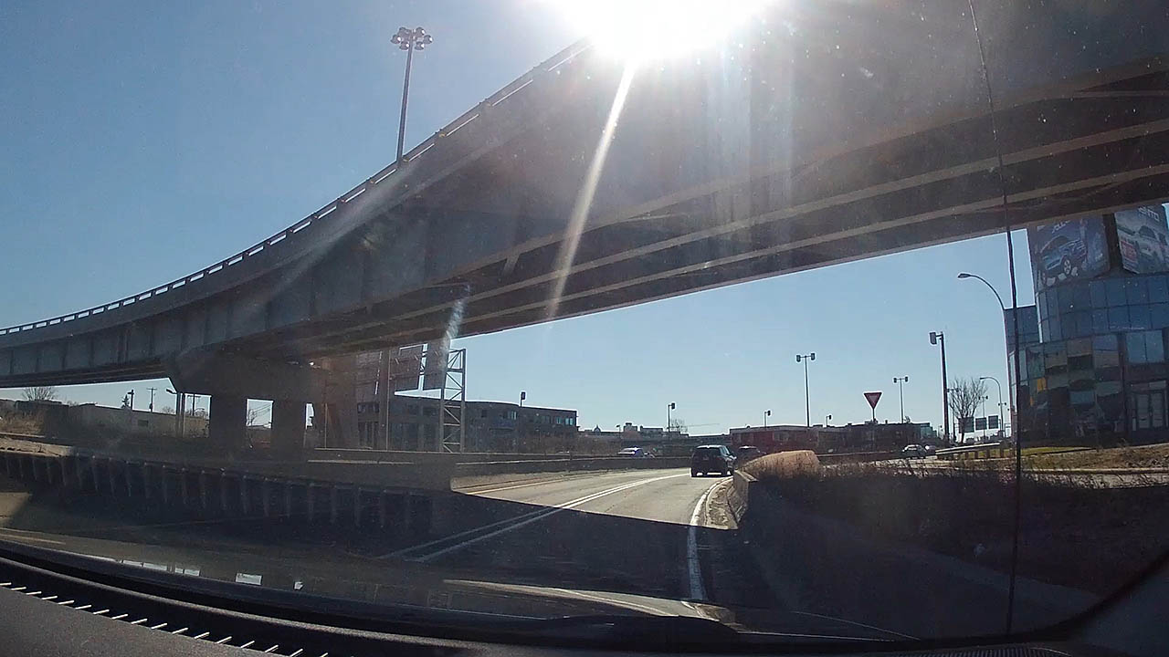 The photograph is a view through the windsheild the GoPro Hero 4 Black camera is mounts to with the GoPro suction cup, outward of the highway with another car and an over pass in Montreal.