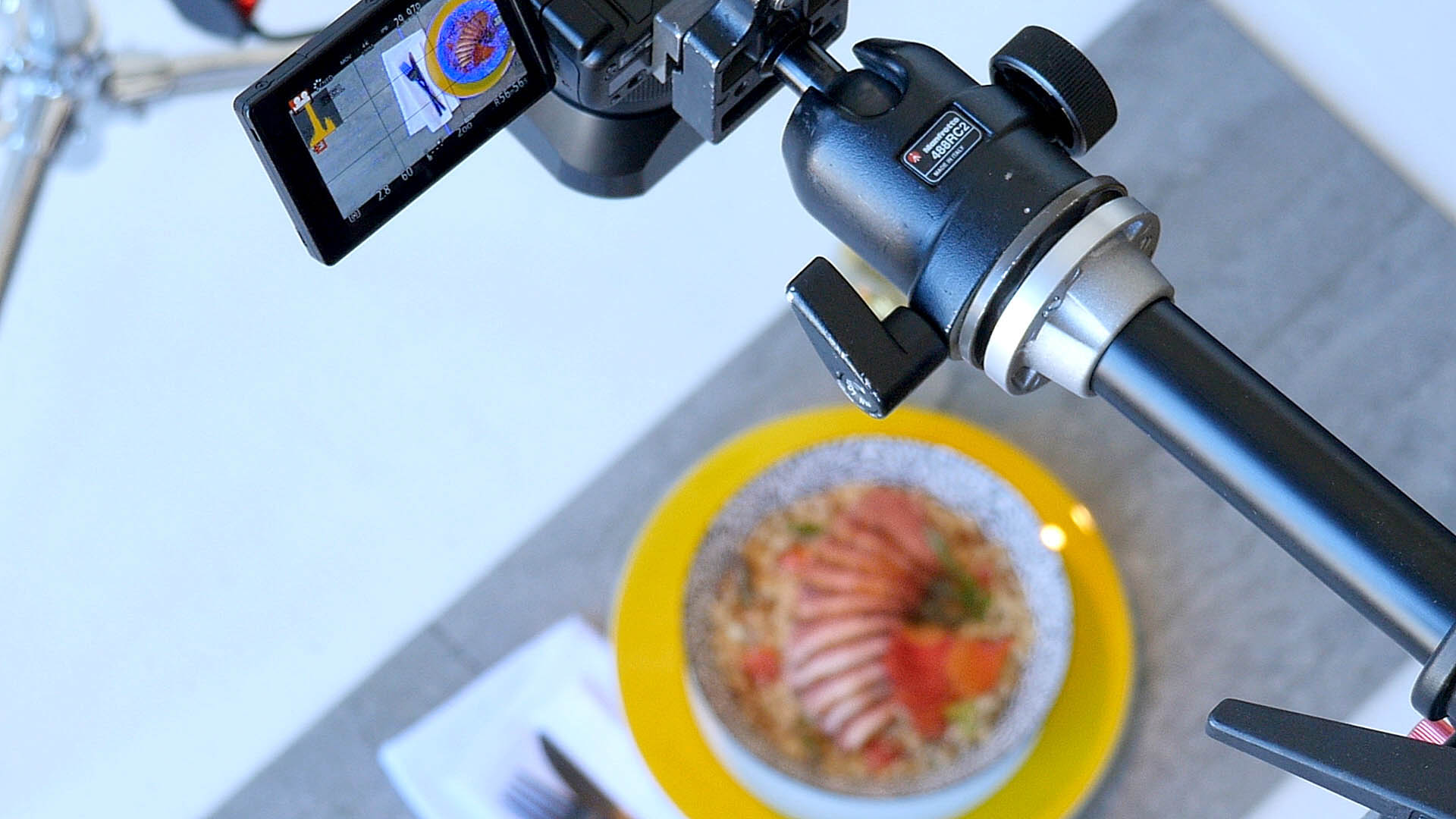A frame grab photograph from the video Food & Camera Gear Behind the Scenes at a Food Photo Video Shoot at a Montreal Studio. The photograph shows a camera pointed down over a beautifully styled bowl of food. The bowl of food is visible in the LCD display on the camera. The camera is a Panasonic GH4 with a Panasonic 25mm f 1.4 lens. Original Food & Camera Gear Behind the Scenes at a Food Photo Video Shoot at a Montreal Studio video posted here https://www.youtube.com/watch?v=Fz8r8y5M-uc